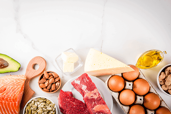 avocado. salmon, nuts, red meat, cheese, eggs, and oil all in raw form on table