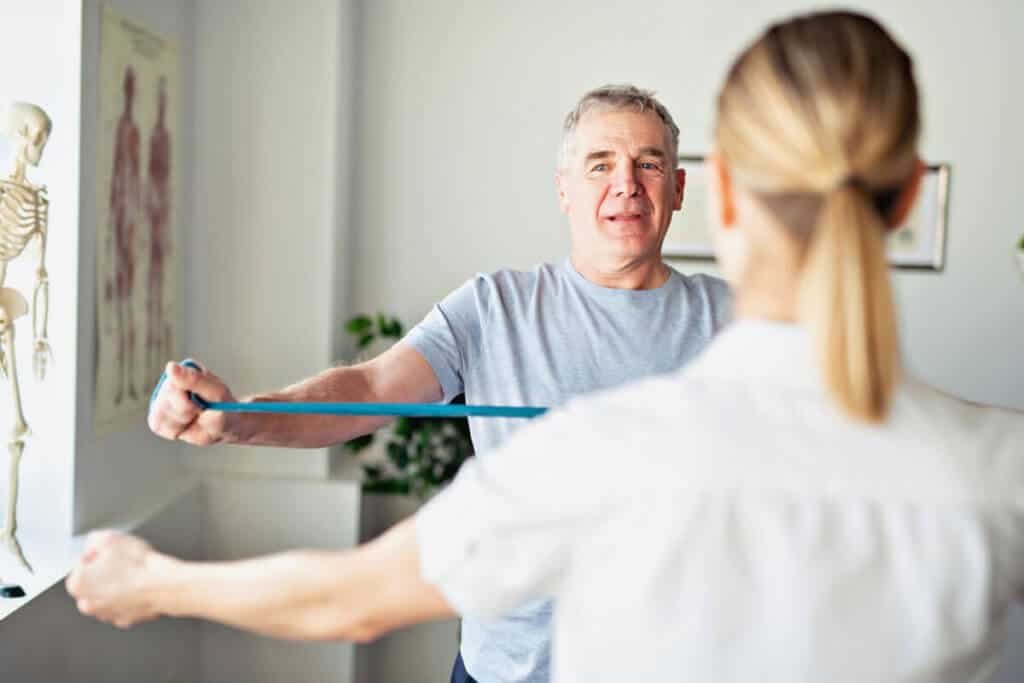Physiotherapists and patient using a band to strength out arms