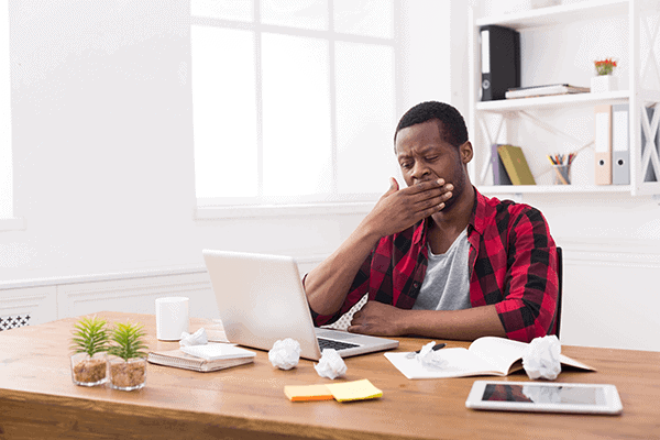 Man working on a laptop yawning 