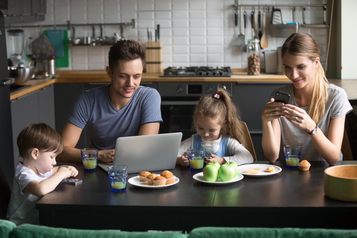 family sitting around a table using phones and computers