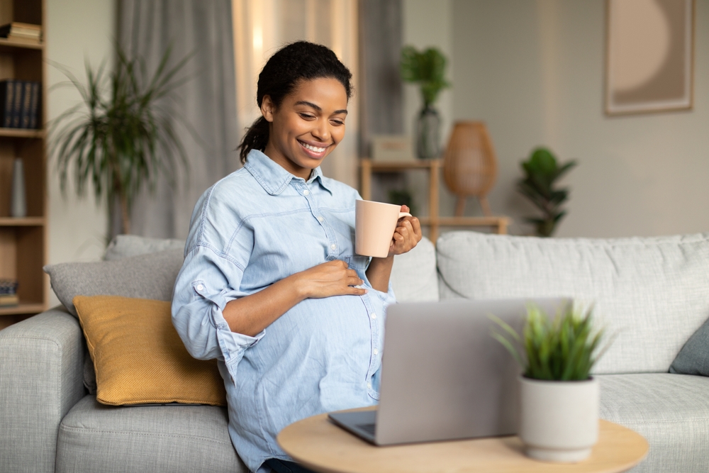 pregnant woman holding a mug using a laptop