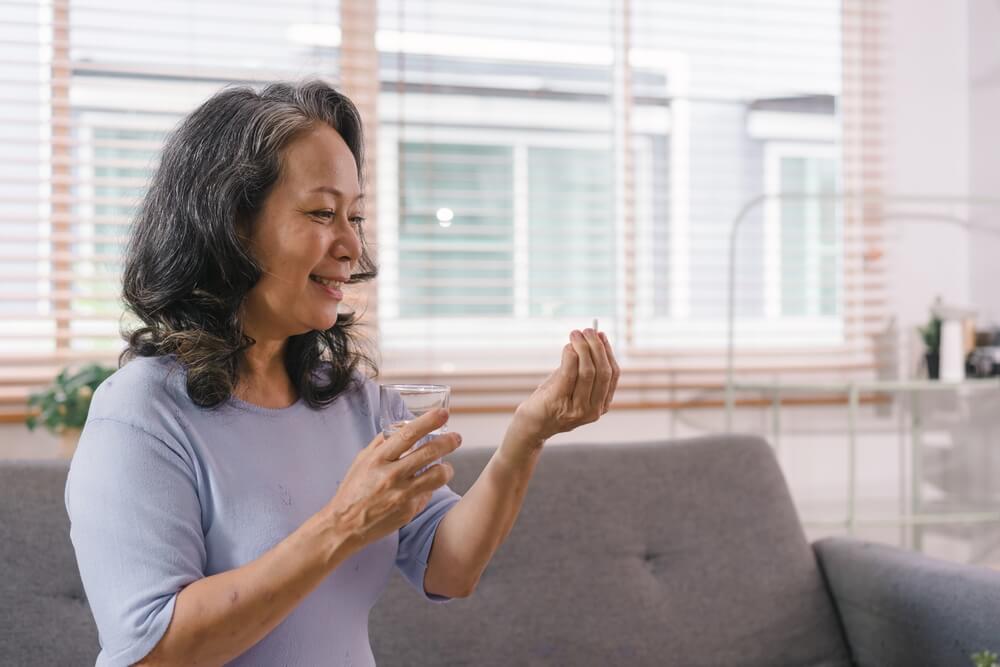 woman holding a glass of water and a supplement