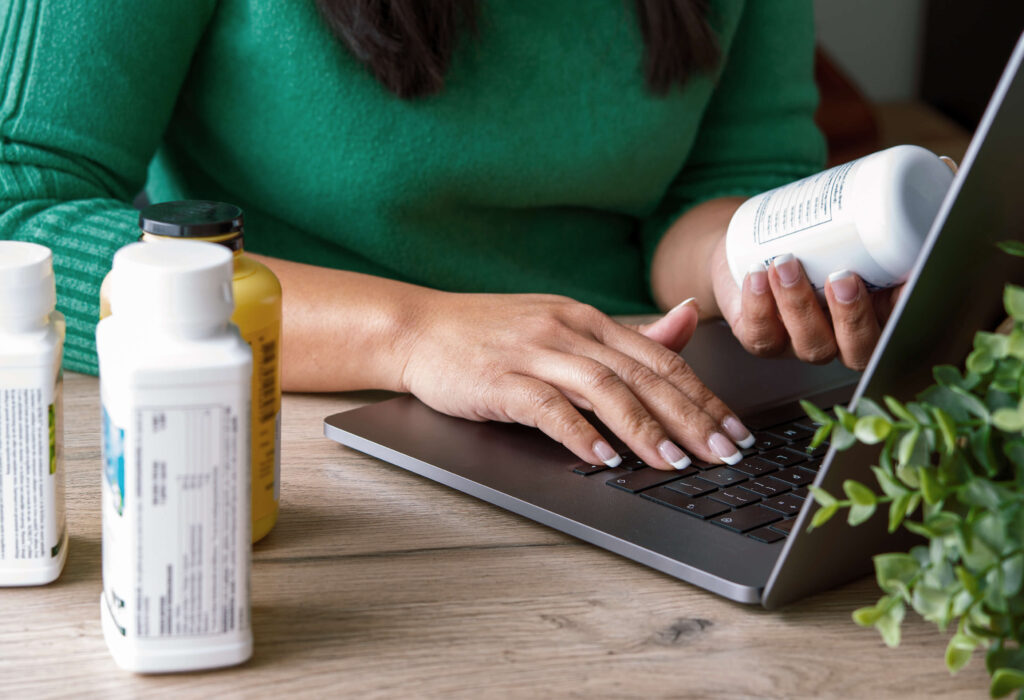 person holding a supplement bottle and using a computer