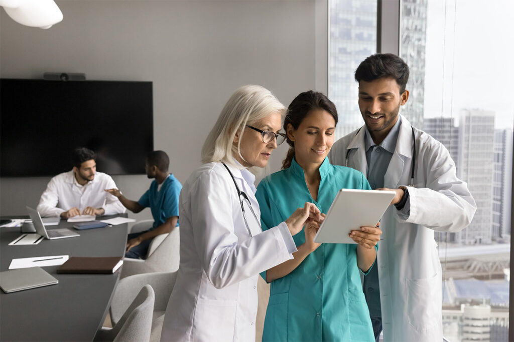 A group of individuals in white coats are gathered indoors, attentively looking at a tablet.